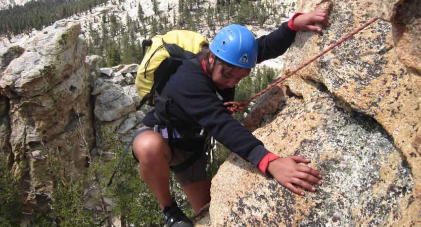 a person wearing safety gear and secured by ropes rock climbs high above the trees below